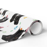 A roll of wrapping paper featuring a playful pattern of black and white dog head and colorful paw prints, shown on a clean white background.