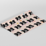 A roll of wrapping paper featuring a repeating pattern of black and white dog faces on a pale pink background, with small colorful heart and paw prints, shown on a white studio background.
