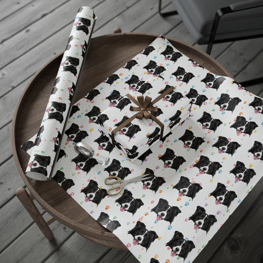 White wrapping paper with a repeating black and white dog print and small colorful heart accents, shown wrapped around a gift box and a matching rolled sheet on a round wooden table. A gift bag, ribbon, and scissors are also visible.